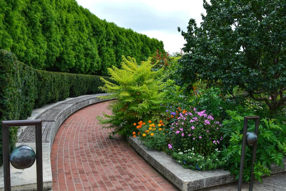 Curved brick path beside a stone planter overflowing with flowers